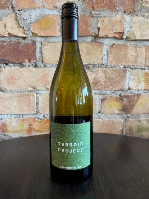 Wine bottle with  a green label with text saying 'Terroir Project' in front of a brick surface