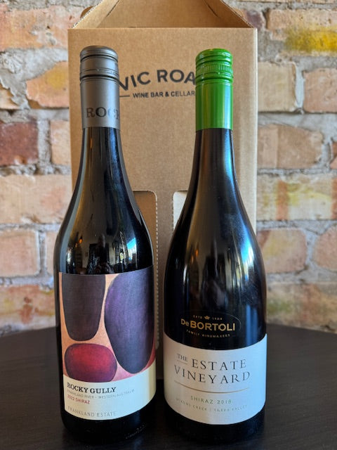 Two wine bottles on a cardboard box with a brick wall background