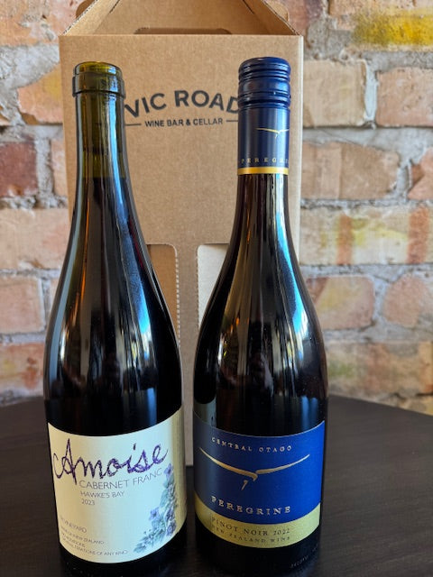 Two wine bottles on a cardboard box with a brick wall background