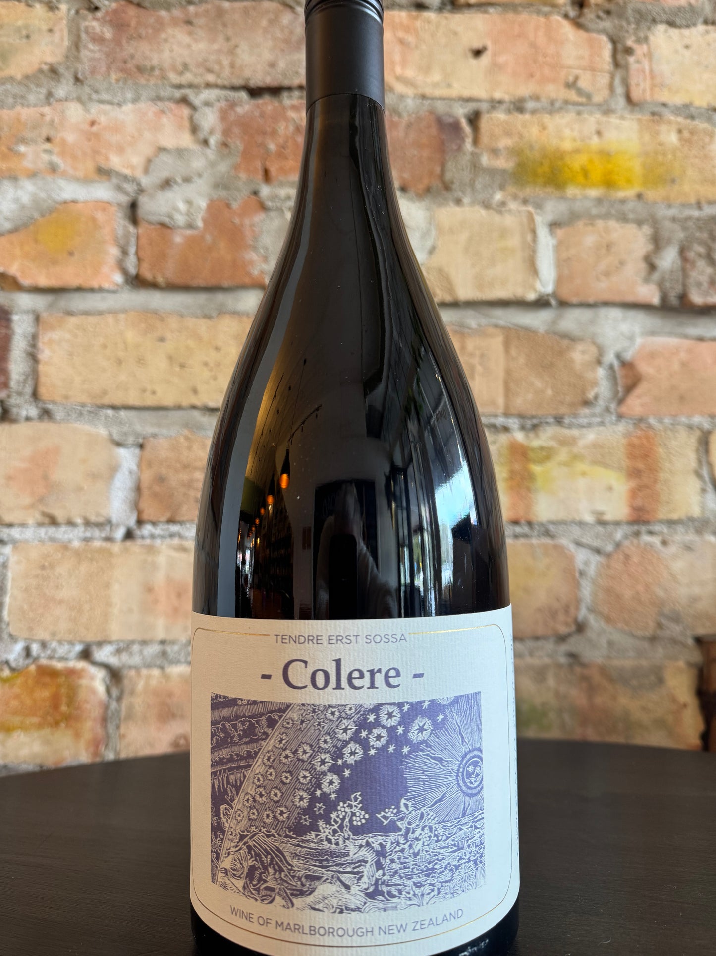 Wine bottle labeled 'Colere' against a brick wall background